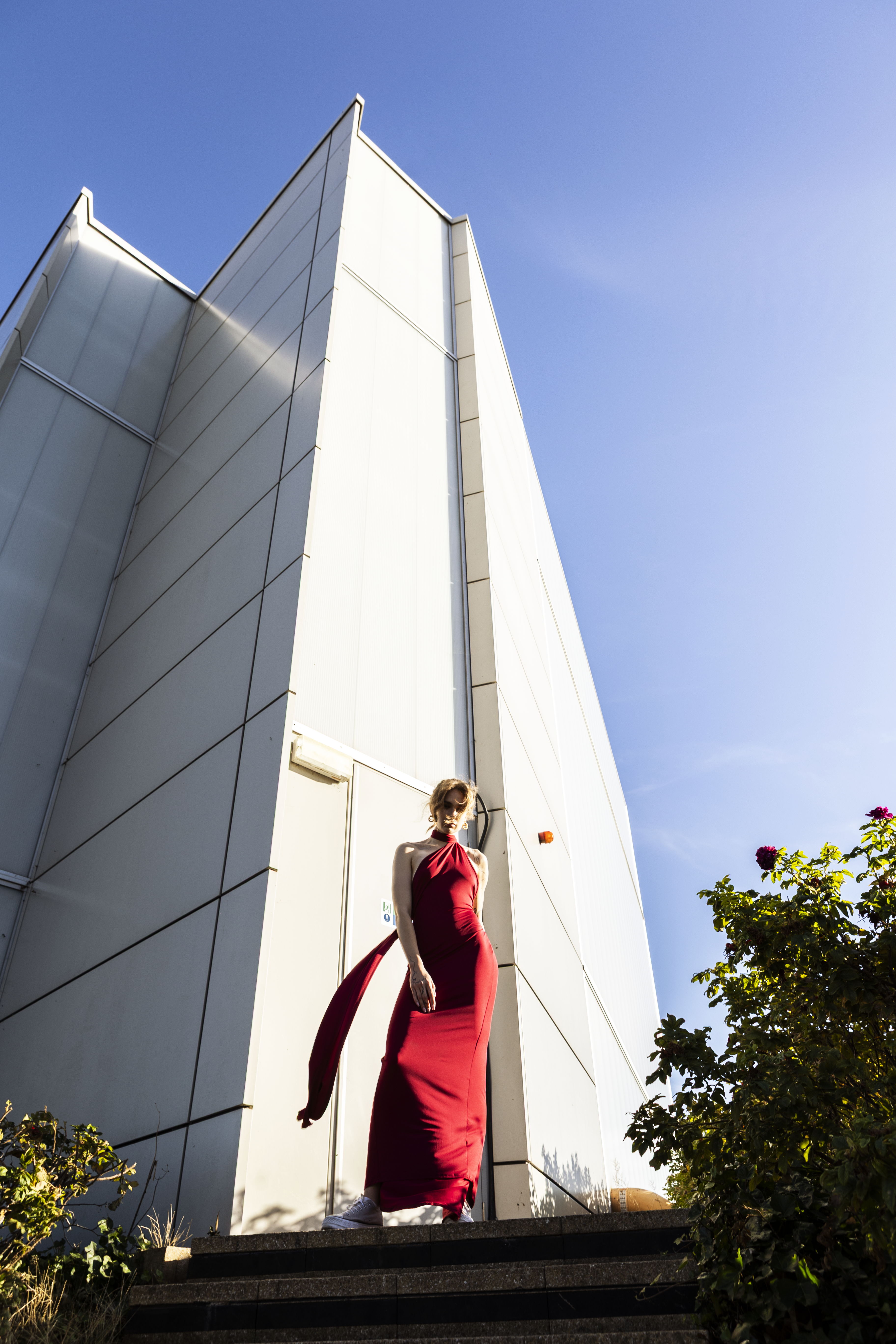 A girl in a red dress stands in front of a tall white building