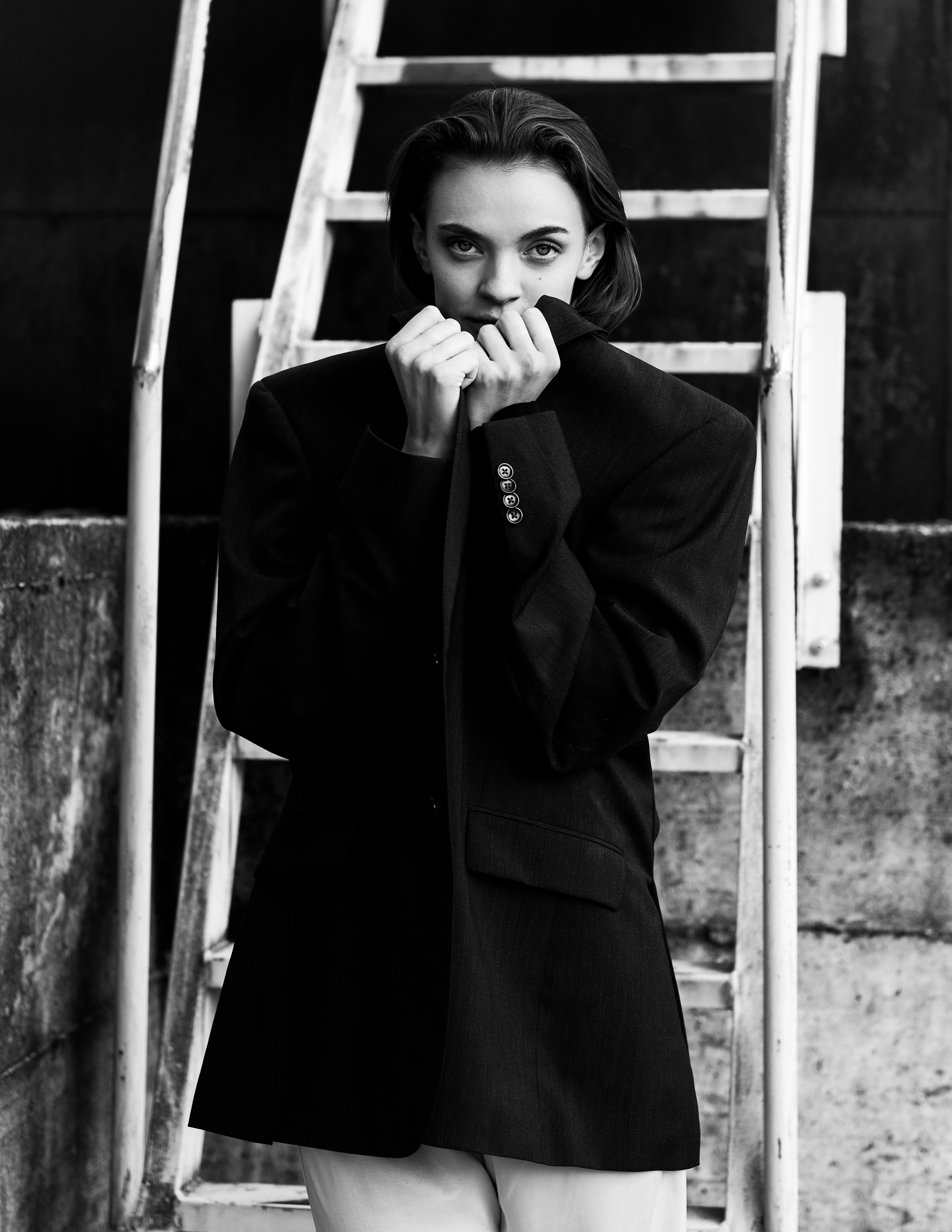 Girl in a blazer stands in front of some old wooden stairs