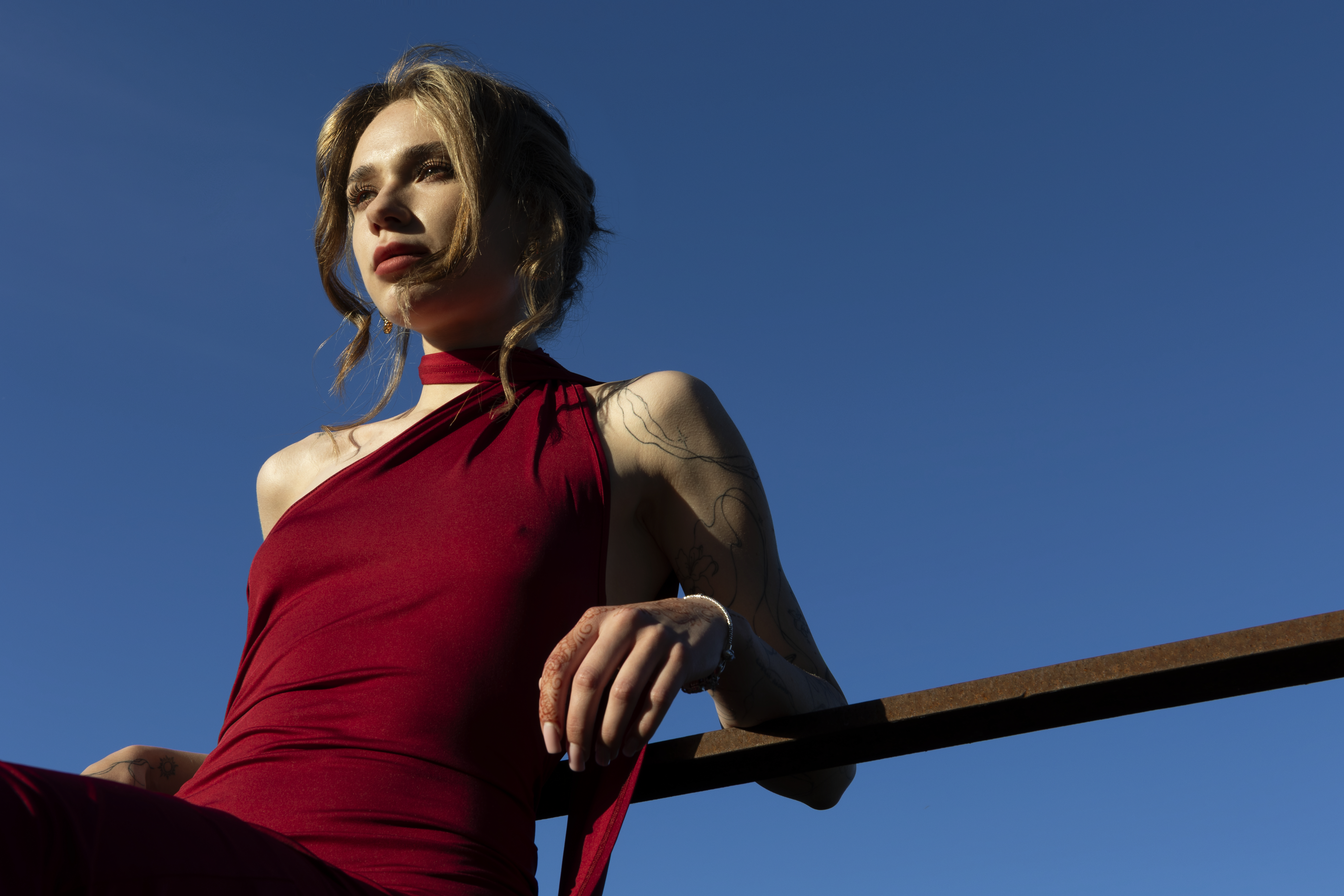 A girl in a red dress sits against a bronzed metal bar.